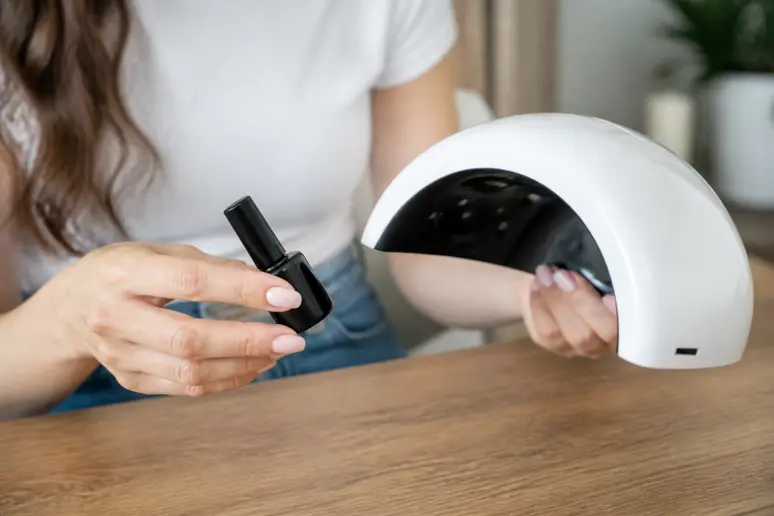 Gros plan sur des mains féminines tenant une lampe UV et un vernis, prudence dans la pose de french manucure semi permanent.