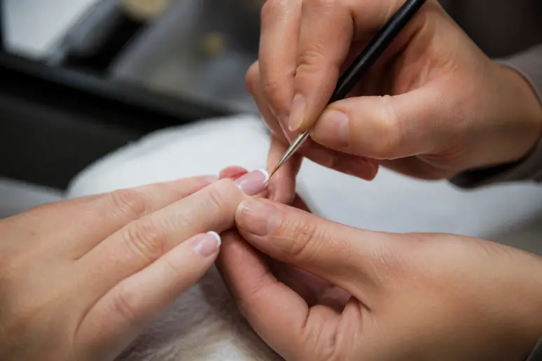 Main traçant une ligne blanche précise pour une french manucure sur ongle court