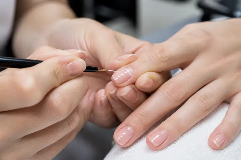 Application minutieuse d'un trait blanc fin sur des ongles courts pour une french manucure classique