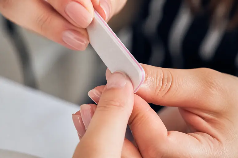 Détail de mains polissant délicatement un ongle naturel avant une manucure américaine Gel-X.