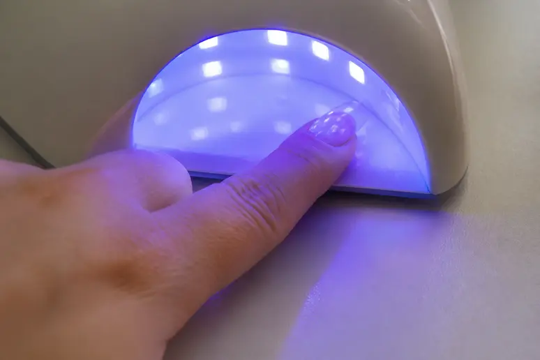 Mains plaçant un ongle sous lampe UV/LED pour la polymérisation d'une manucure américaine.