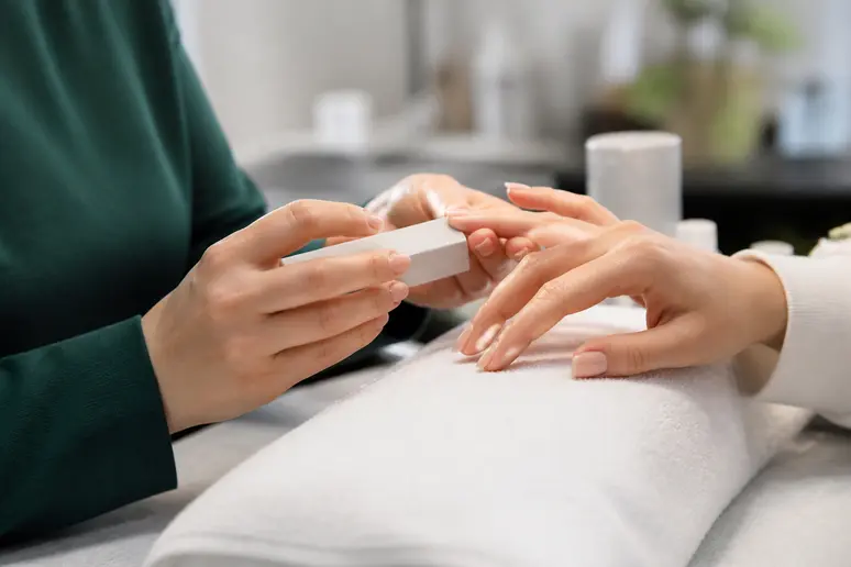 Mains d'une esthéticienne réalisant un polissage doux des ongles fragiles lors d'une séance de manucure chinoise en institut.