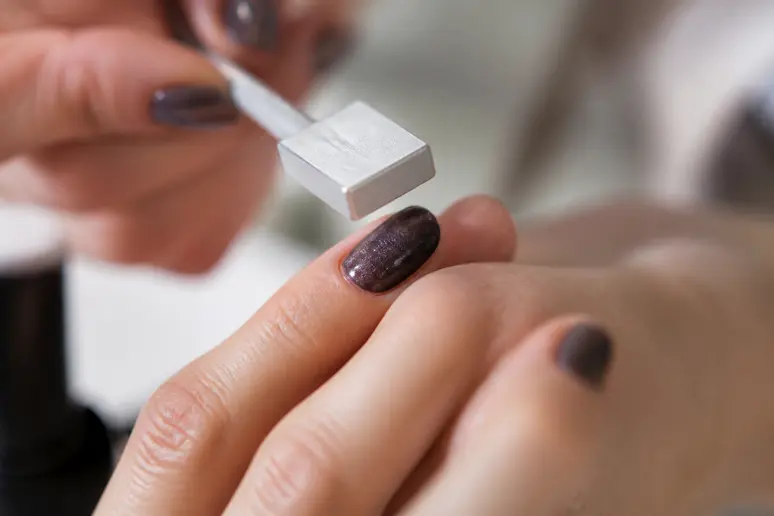 Mains créant l'effet œil de chat sur un ongle avec un aimant et un vernis magnétique.