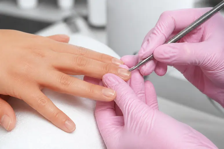 Manucure minutieuse repoussant les cuticules d'un ongle rongé avant la pose