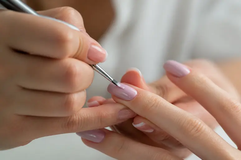 Application minutieuse d'un vernis pour réussir une manucure pastel soignée.