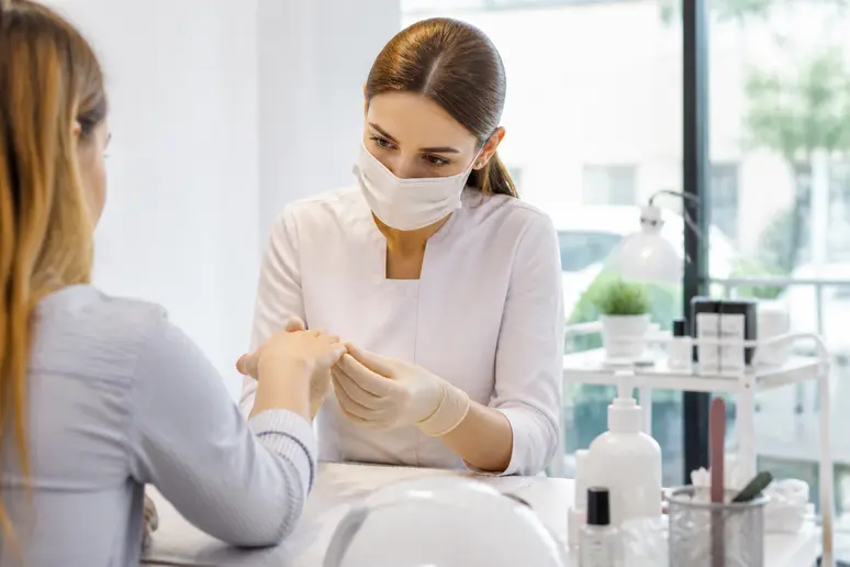 Praticienne en gants stériles examinant les mains d'une cliente pour une manucure sécurisée