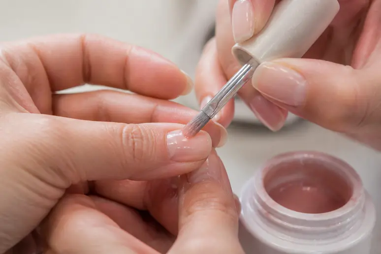 Main d'une prothésiste appliquant une résine pour nail art formation.