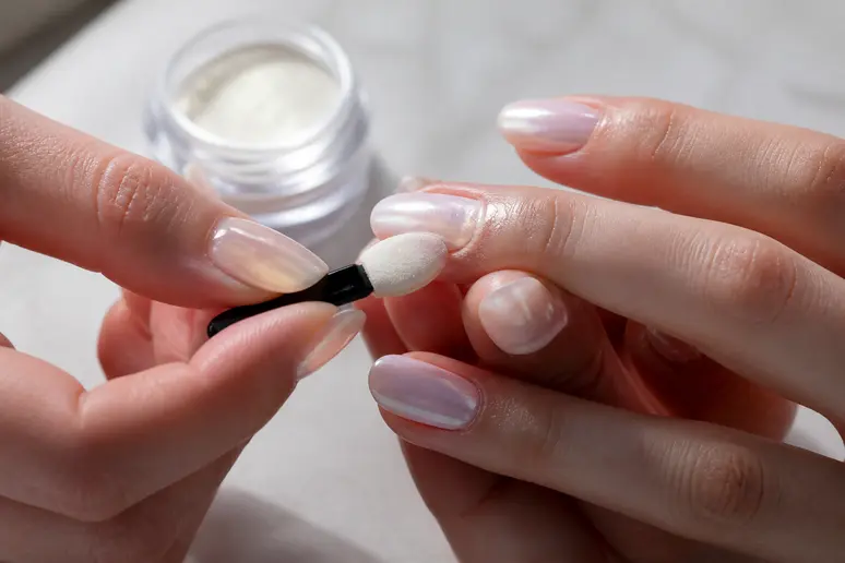 Application d'une poudre chromée sur les ongles pour réaliser un effet glazed donut brillant.