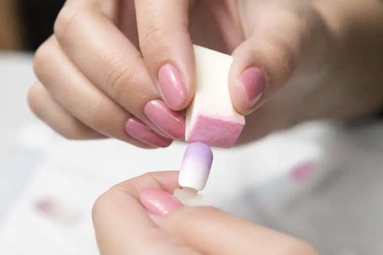 Mains créant un dégradé de nail art Octobre Rose avec une éponge.