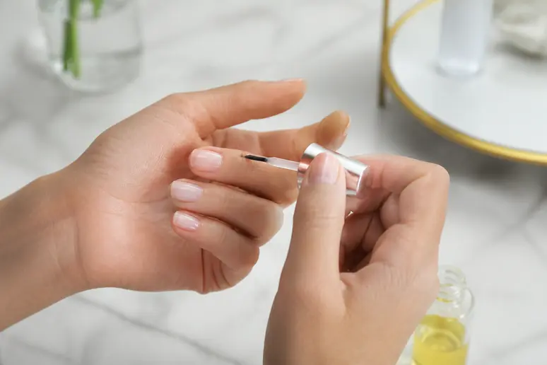 Application d'huile autour des cuticules pour protéger la peau avant un nail art tendance 2026.