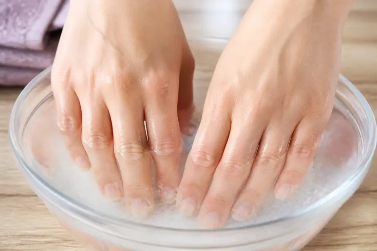 Mains trempant dans un bain salé pour renforcer les ongles cassants, remède de grand-mère efficace.