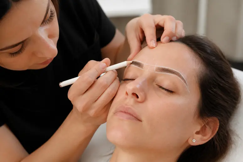 Praticienne traçant les repères précis pour une épilation définitive sourcil sur une cliente.