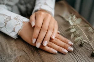 Mains de mariée avec une manucure mariage boheme délicate posées sur une table en bois rustique
