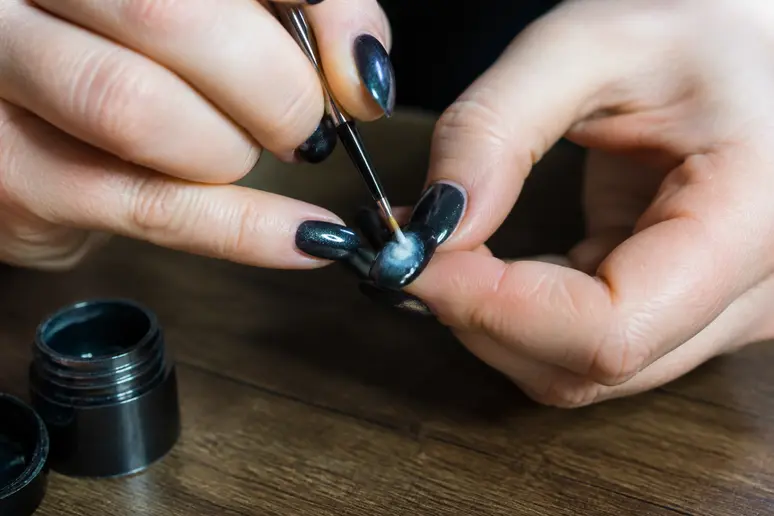 Application d'un nail art aura sur base foncée avec un pinceau fin pour un design de janvier