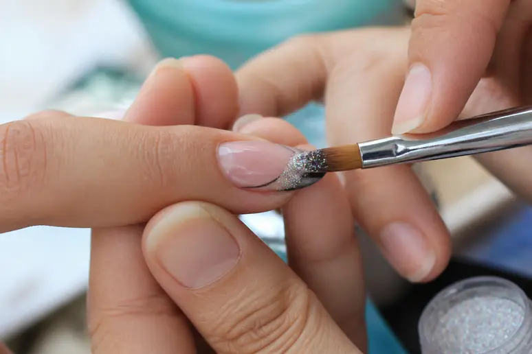 Application minutieuse de paillettes fines sur les ongles avec un pinceau plat.