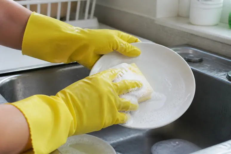 Mains portant des gants de ménage pendant la vaisselle pour éviter les ongles fragiles