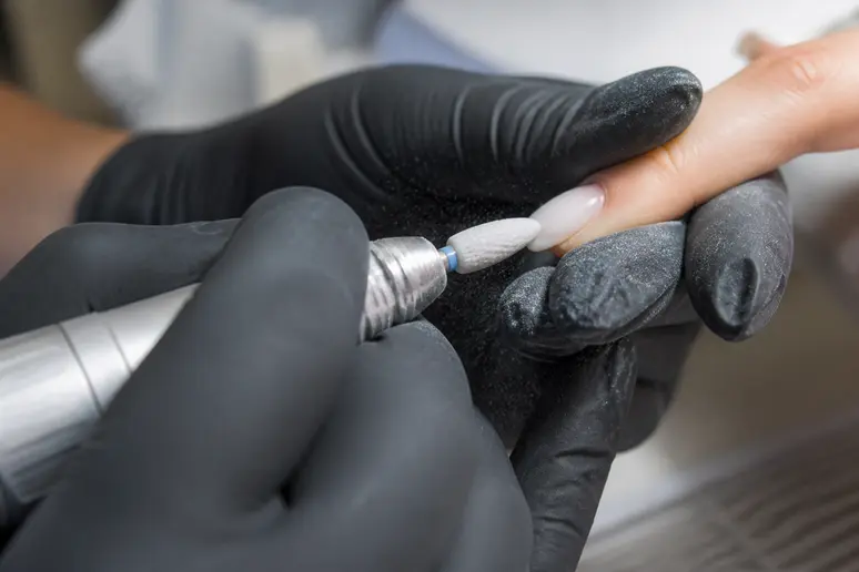 Mains d'une prothésiste ongulaire positionnant une ponceuse à plat sur un ongle.